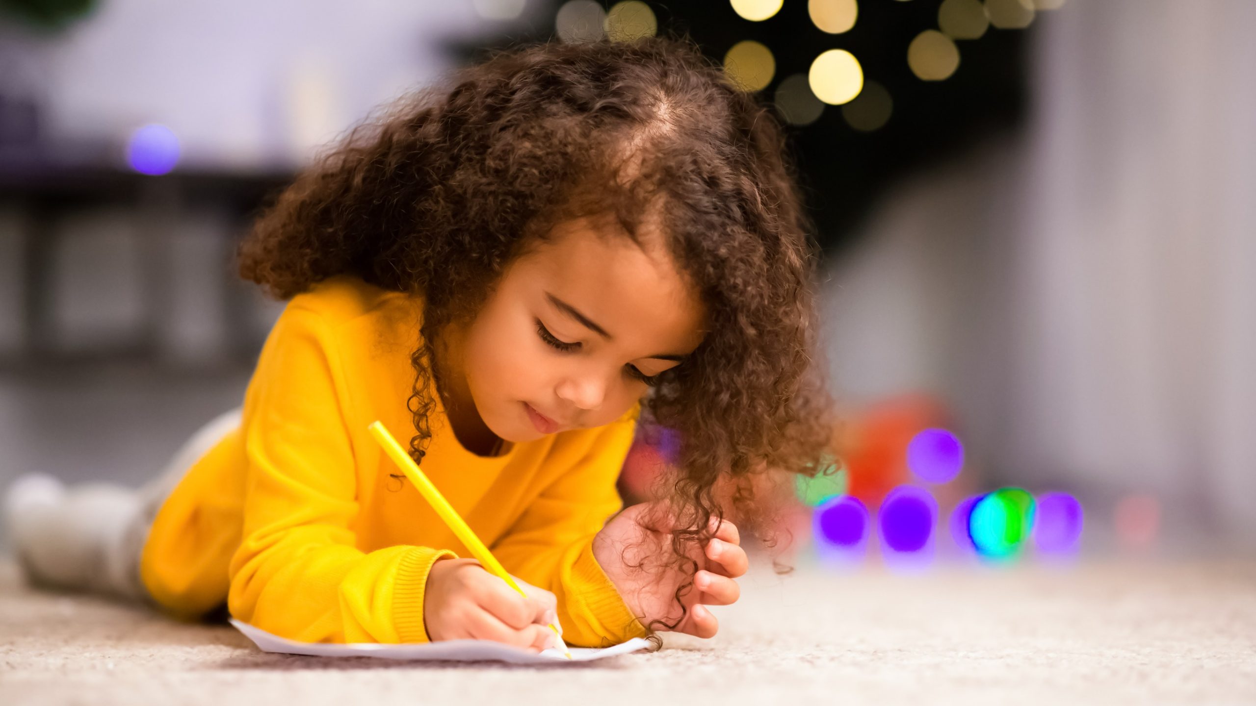 Little girl coloring a piece of paper with a colored pencil.