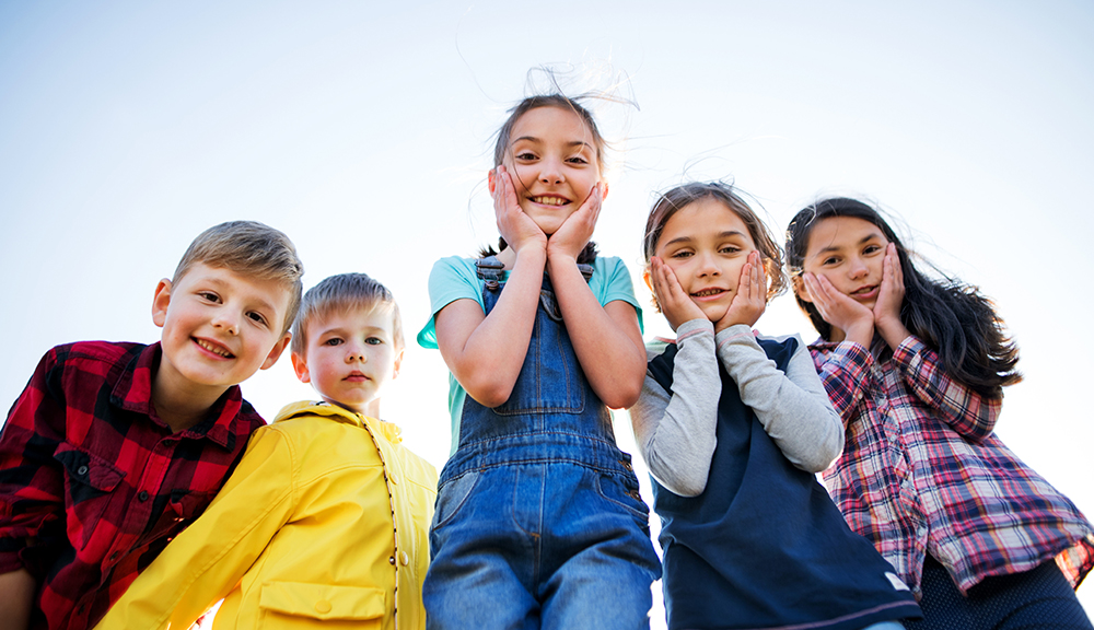 Group of school children standing on field trip in nature, looking at camera.